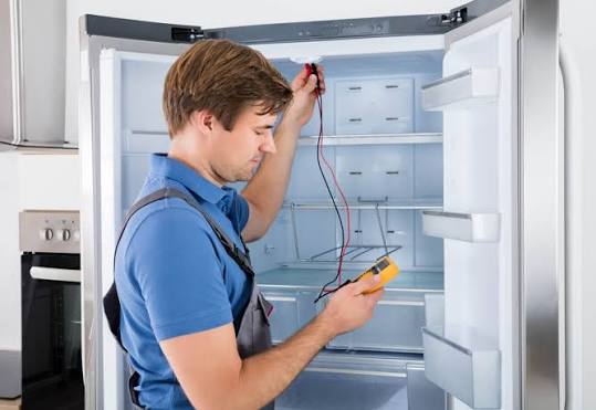 Technician testing the interior electrical components of an open refrigerator